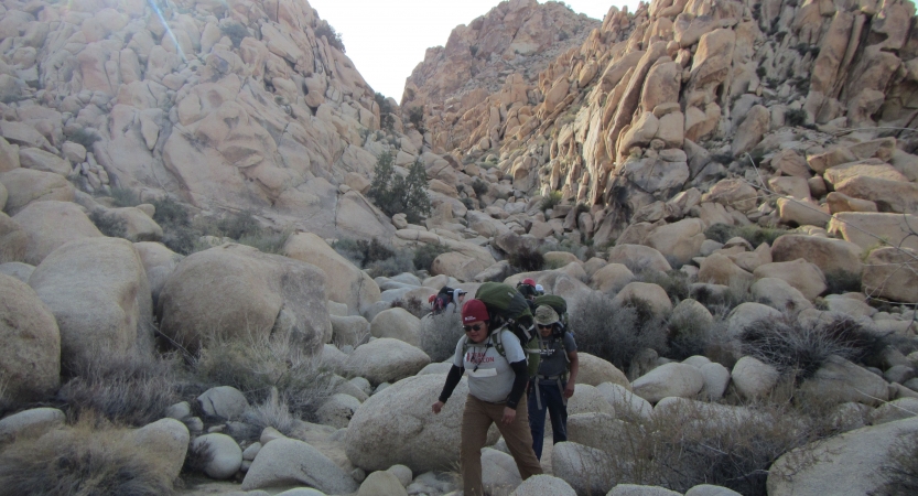 Backpackers hike through rocky terrain and large rock formations. 